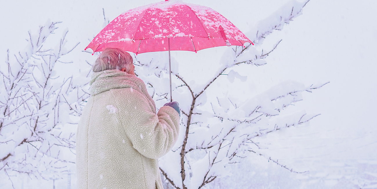 older woman with white jacket and red umbrella back with snowy background